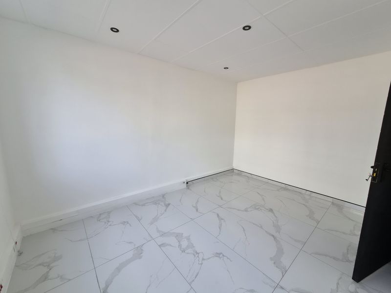 A bright, vacant office space featuring modern marble-look floor tiles, recessed downlighting, and a clean, neutral finish throughout.