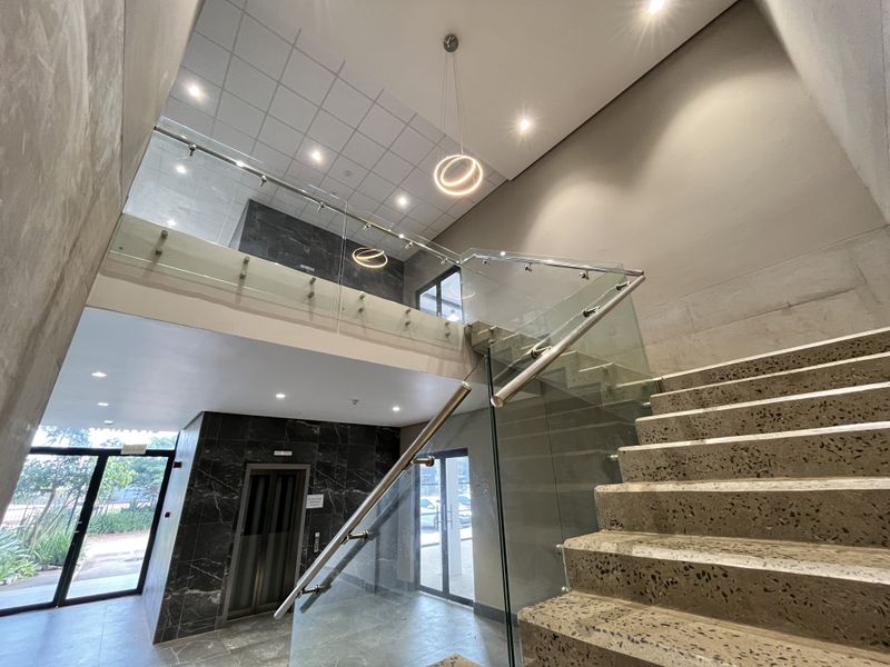 Modern commercial lobby featuring a striking terrazzo staircase, glass balustrades, marble-look wall cladding, and contemporary pendant lighting.