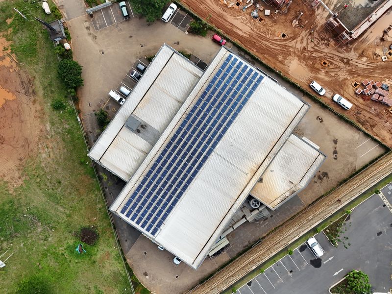 Aerial view of a commercial property featuring a large metal roof equipped with an extensive solar panel array and adjacent paved parking areas.