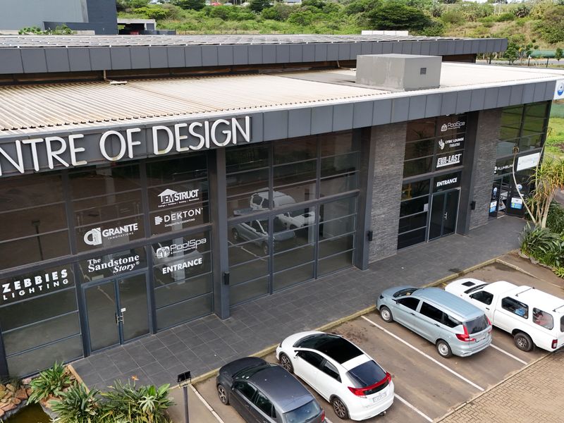 Aerial view of the Centre of Design retail complex, featuring modern glass facade, signage, and paved parking area.