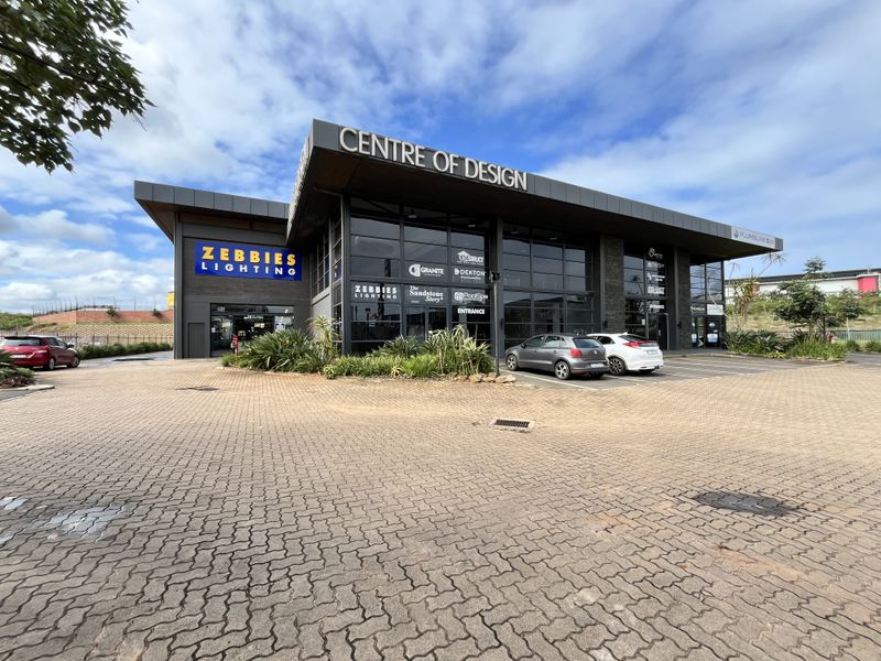 Modern commercial retail building facade featuring large glass storefronts, paved parking area, and prominent signage for multiple tenants.