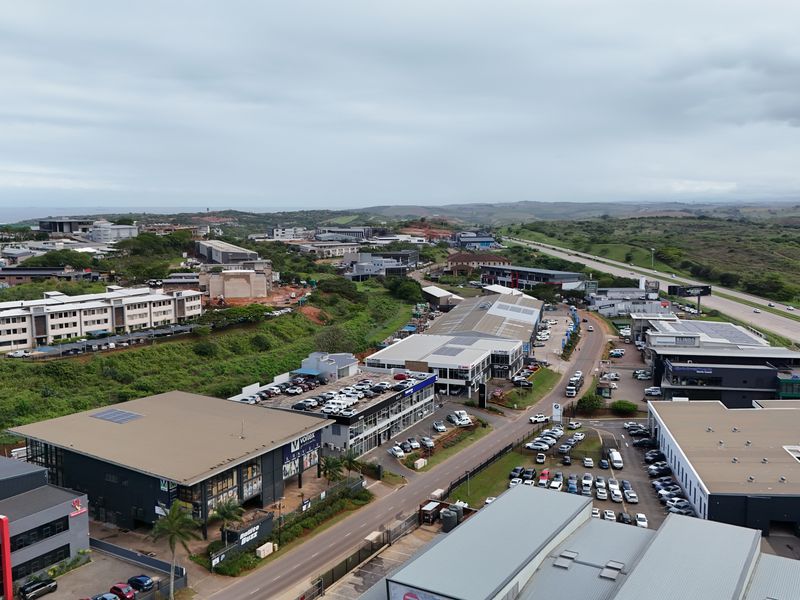 Aerial view of a commercial retail and business park area featuring multiple modern buildings, parking facilities, and surrounding landscape.