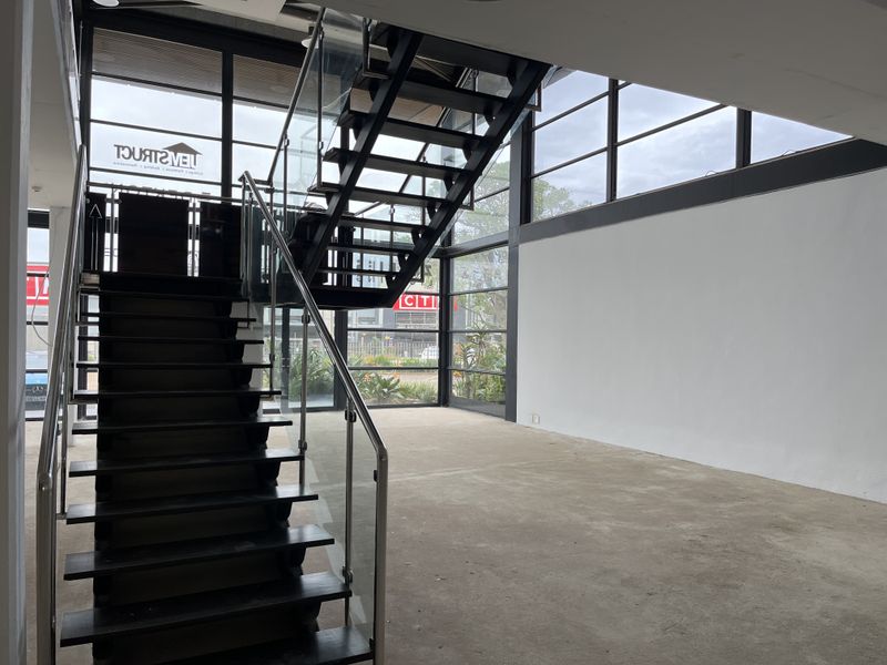 Modern open-plan retail space featuring a striking black steel staircase with glass balustrades and expansive floor-to-ceiling windows providing excellent natural light.