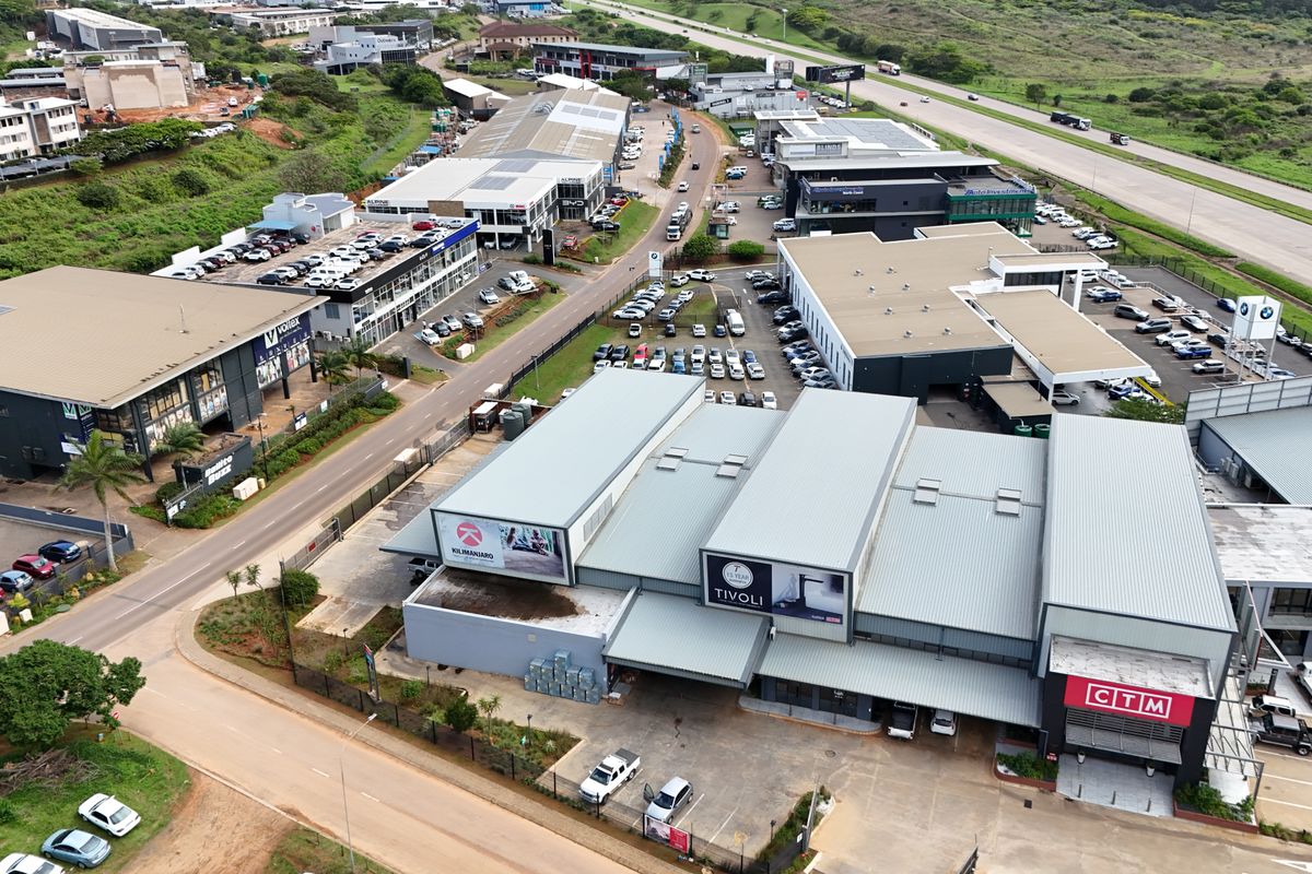 Aerial view of a commercial retail park featuring multiple warehouse-style buildings, paved parking areas, and convenient access to the main road.