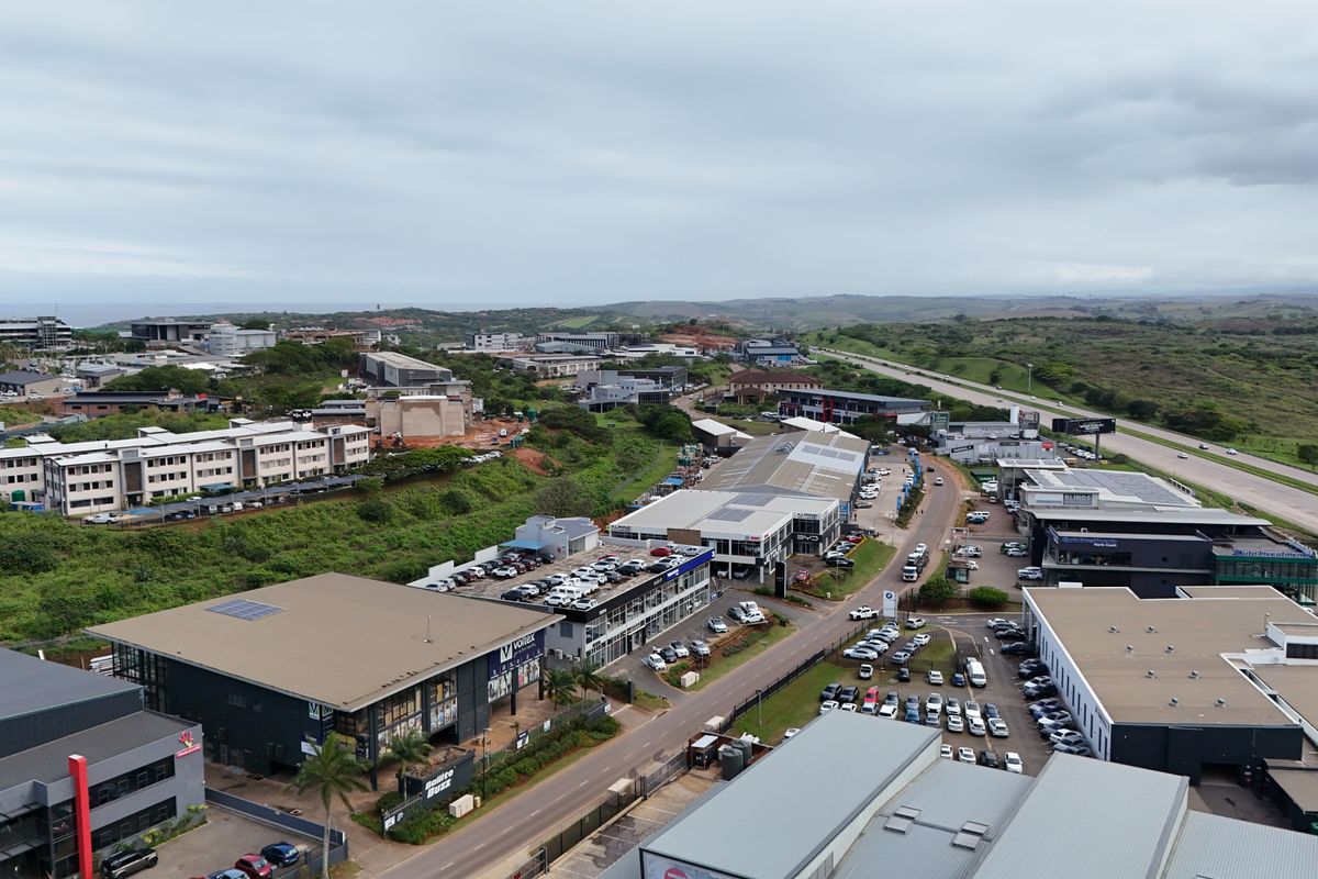 Aerial view of a commercial retail and business park area featuring multiple modern buildings, parking facilities, and surrounding landscape.