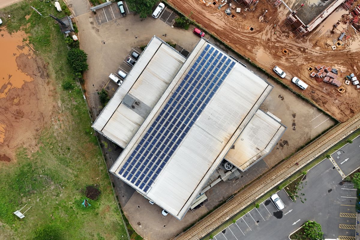 Aerial view of a commercial property featuring a large metal roof equipped with an extensive solar panel array and adjacent paved parking areas.
