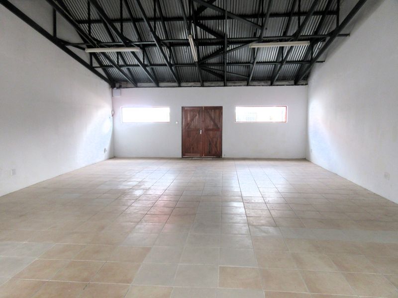 A spacious, empty commercial utility area featuring exposed steel roof trusses, tiled flooring, and double timber doors, suitable for various business or storage uses.