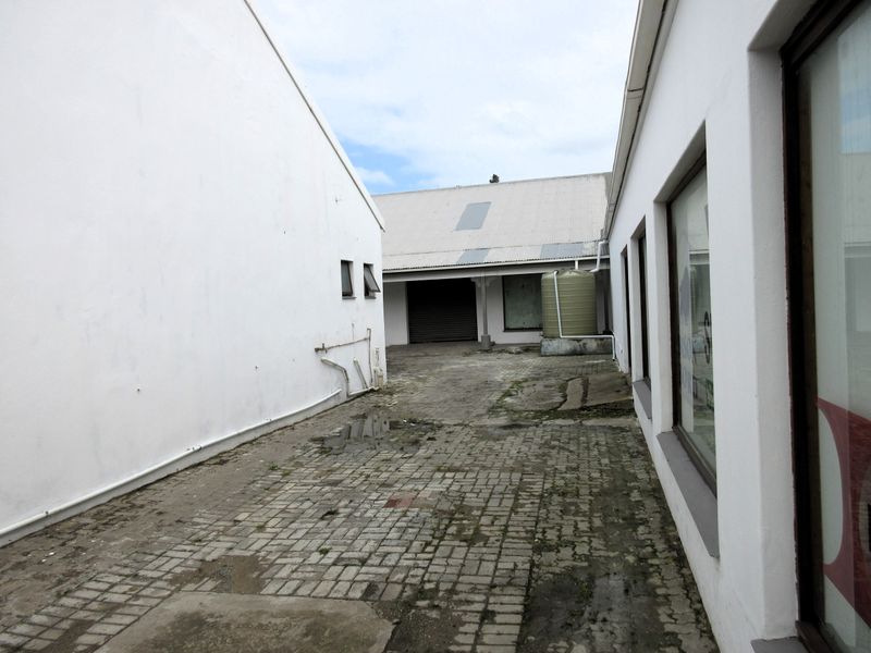 Rear exterior courtyard area featuring paved ground, a water storage tank, and access to a commercial building with a roller shutter door.