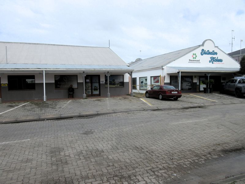 Front view of a commercial property featuring two adjacent buildings with corrugated metal roofs, paved parking, and prominent business signage.