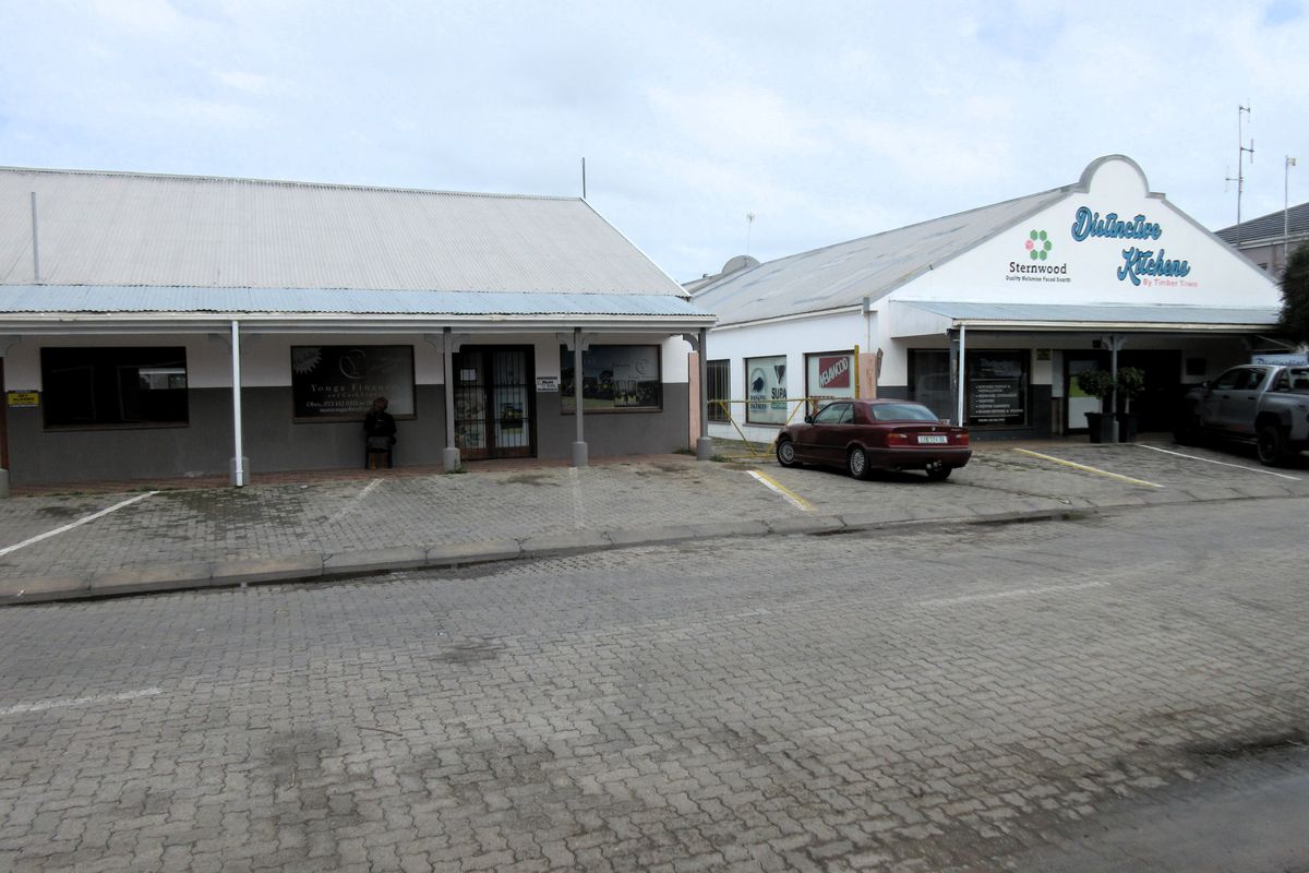 Front view of a commercial property featuring two adjacent buildings with corrugated metal roofs, paved parking, and prominent business signage.