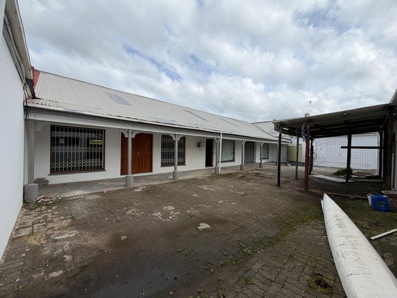 Rear exterior view of a commercial property featuring a paved courtyard, covered veranda, and secure access points with metal security gates.