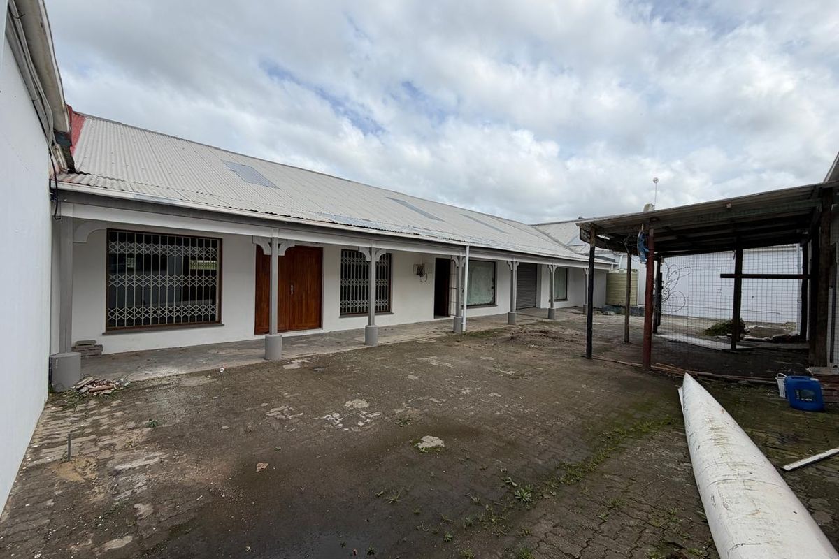 Rear exterior view of a commercial property featuring a paved courtyard, covered veranda, and secure access points with metal security gates.