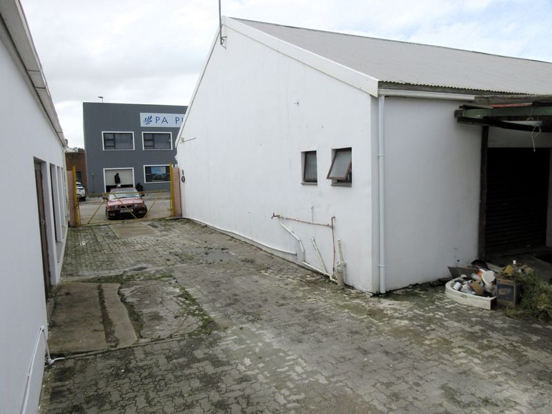 Rear exterior view of the commercial property featuring a paved yard area, corrugated metal roofing, and external utility connections.