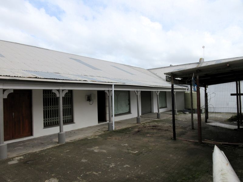 Rear exterior view of a commercial building featuring a covered walkway, corrugated metal roofing, security gates, and a roller shutter door.