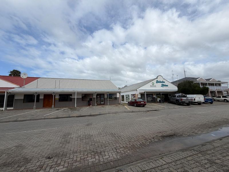 Front exterior view of a commercial property featuring a paved parking area, covered walkways, and prominent signage for the business premises.