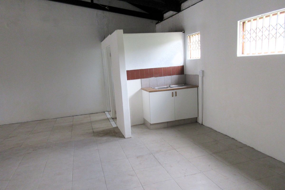 An empty commercial kitchen space featuring tiled flooring, basic base cabinetry with a sink, and security bars on the windows.