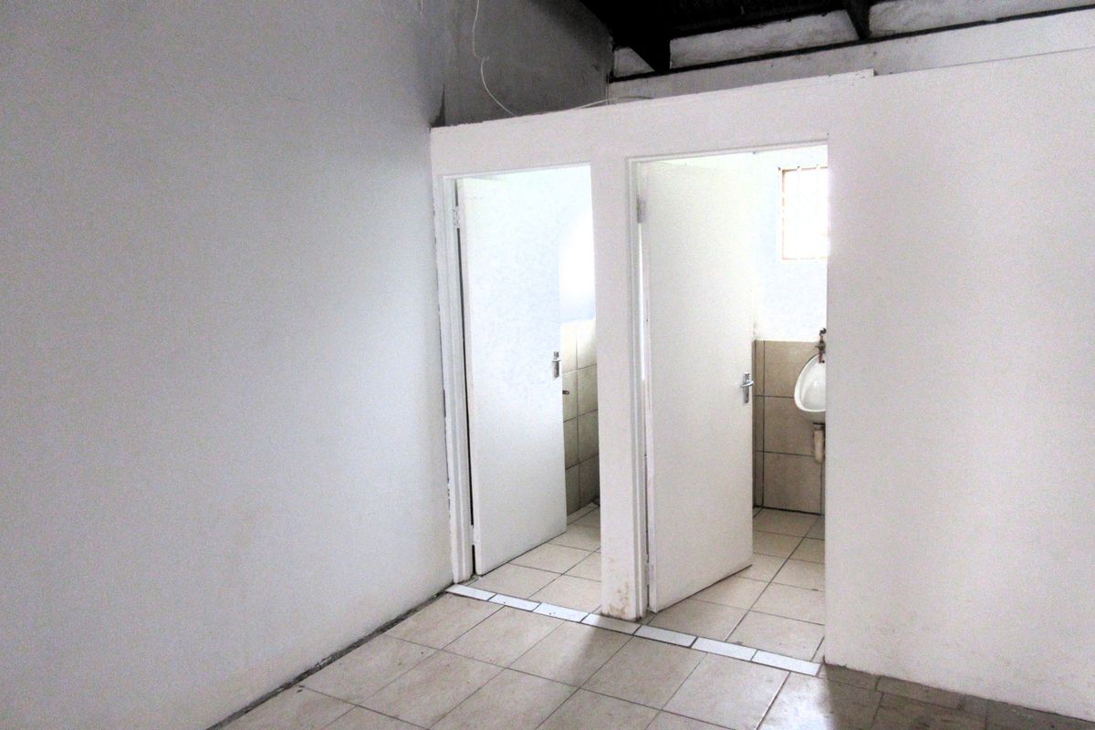 A functional commercial restroom area featuring tiled flooring and multiple partitioned stalls with basic sanitary fixtures.