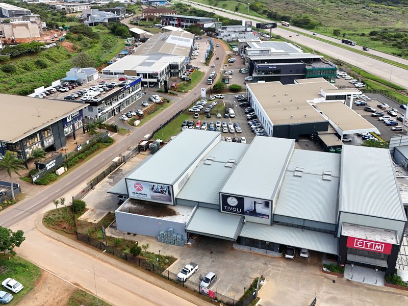 Aerial view of a commercial retail park featuring multiple warehouse-style buildings, paved parking areas, and convenient access to the main road.