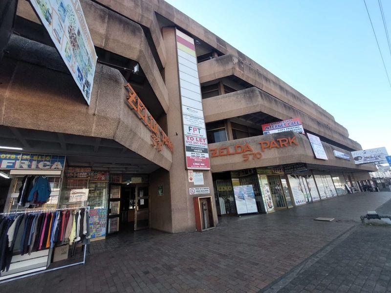 Exterior view of Zelda Park office building featuring multi-level concrete architecture, ground floor retail shopfronts, and prominent street-level signage.