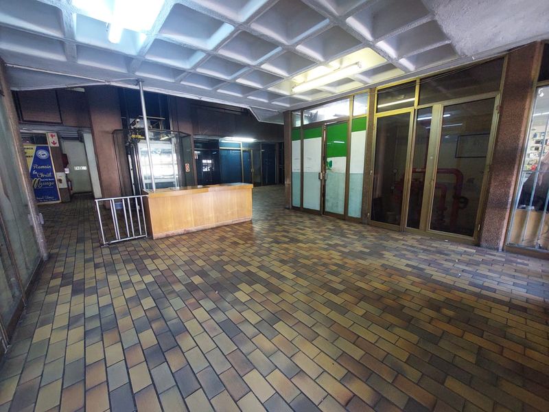 A spacious office building lobby featuring a coffered ceiling, tiled flooring, and a built-in reception counter with glass-paneled office partitions.