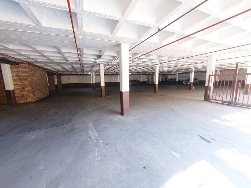 A spacious covered parking garage featuring a waffle slab ceiling, exposed fire sprinkler piping, and brick wall accents.