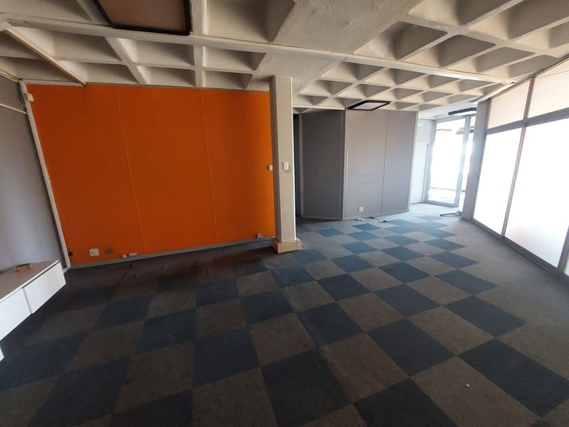An empty office space featuring a coffered ceiling, checkered carpet flooring, and large windows providing natural light.