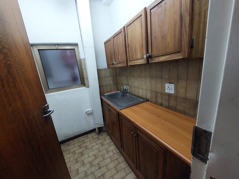 A compact kitchenette or utility area featuring wooden cabinetry, a stainless steel sink, and tiled backsplash.