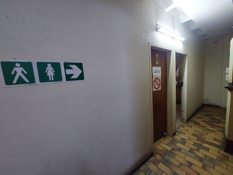 A functional office hallway featuring tiled flooring, directional signage, and access to restroom facilities.