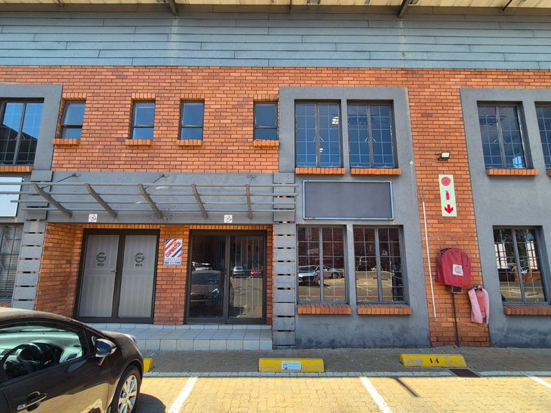 Front elevation of an industrial unit featuring a brick facade, metal-framed windows, glass entrance doors, and dedicated parking bays.