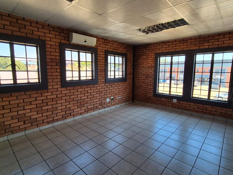 A bright, empty office space featuring exposed brick walls, tiled flooring, a suspended ceiling, and split-system air conditioning.