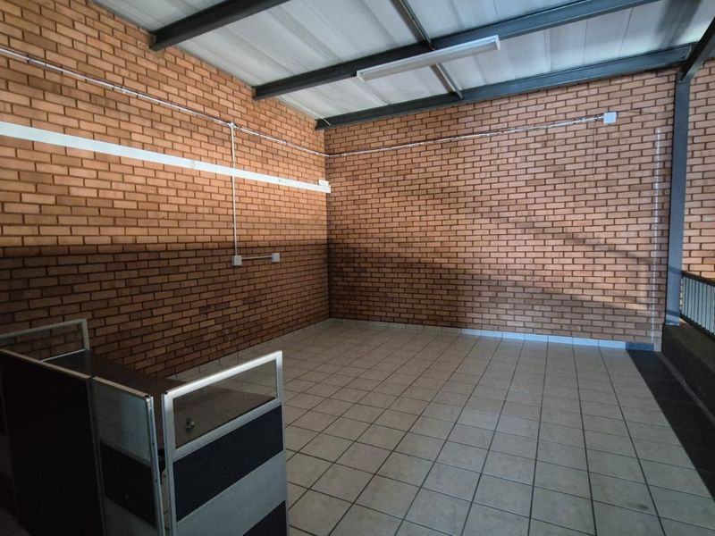 An open-plan industrial office space featuring exposed brick walls, tiled flooring, and exposed steel roof beams, offering a versatile workspace.