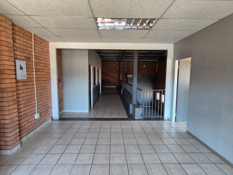 Spacious industrial hallway featuring ceramic tile flooring, exposed brick accents, and a suspended ceiling with integrated lighting, leading to a secure roller shutter access point.