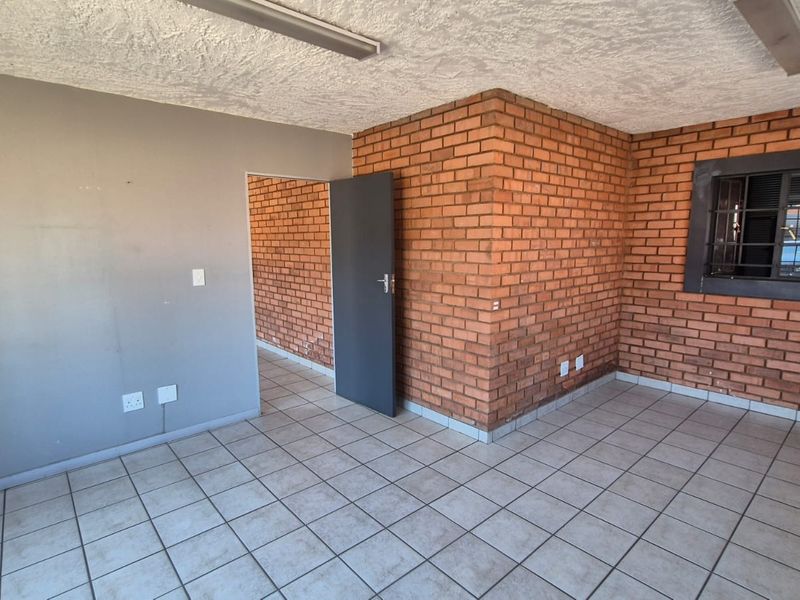 An empty office space featuring exposed brick walls, ceramic tile flooring, and security bars on the window, suitable for industrial or commercial use.