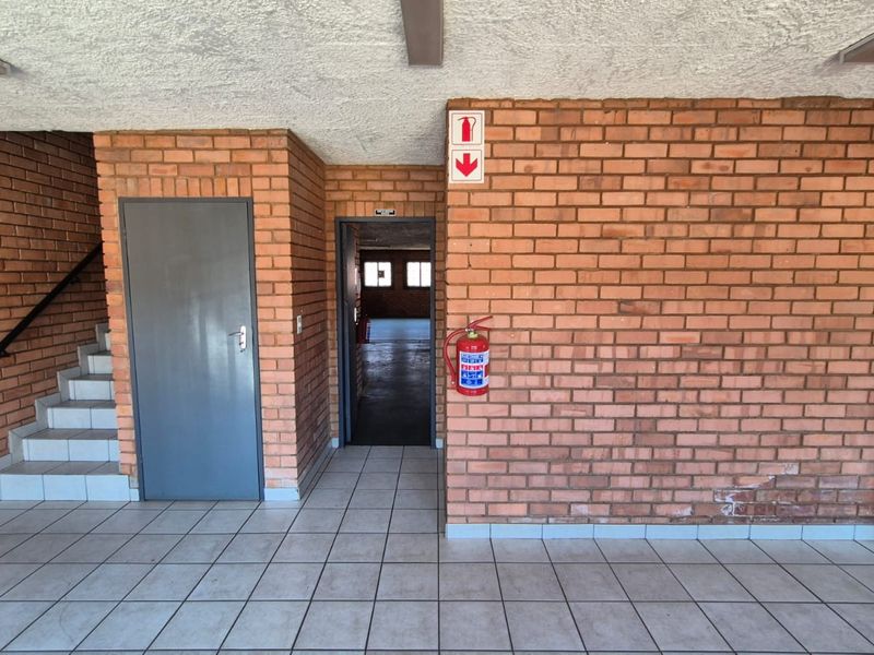 A functional industrial hallway featuring exposed brick walls, tiled flooring, and a staircase, equipped with essential fire safety equipment.