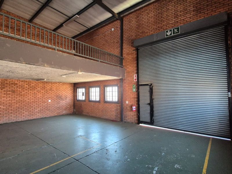 Spacious industrial warehouse unit featuring a large roller shutter door, mezzanine level, exposed brickwork, and durable concrete flooring suitable for various commercial operations.