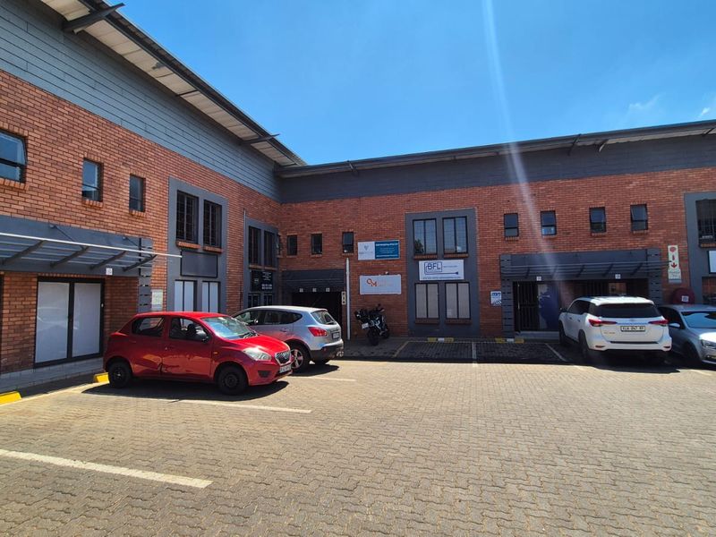 Front exterior view of an industrial office complex featuring brick facade, metal roofing, and dedicated paved parking bays for tenants and visitors.