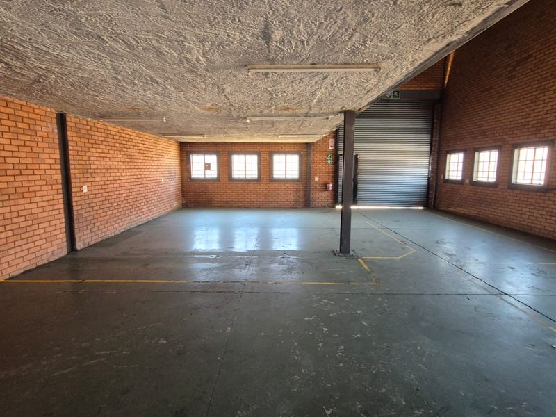 Spacious industrial utility area featuring exposed brick walls, concrete flooring, and a large roller shutter door, suitable for storage or workshop use.