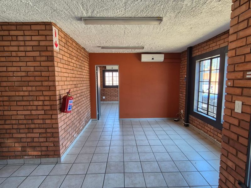 Empty office space featuring exposed brick walls, ceramic tile flooring, split-system air conditioning, and security bars on windows.