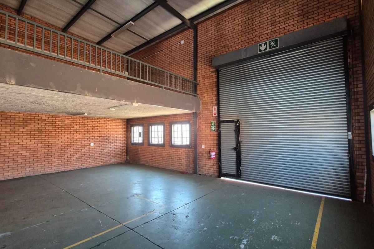 Spacious industrial warehouse unit featuring a large roller shutter door, mezzanine level, exposed brickwork, and durable concrete flooring suitable for various commercial operations.
