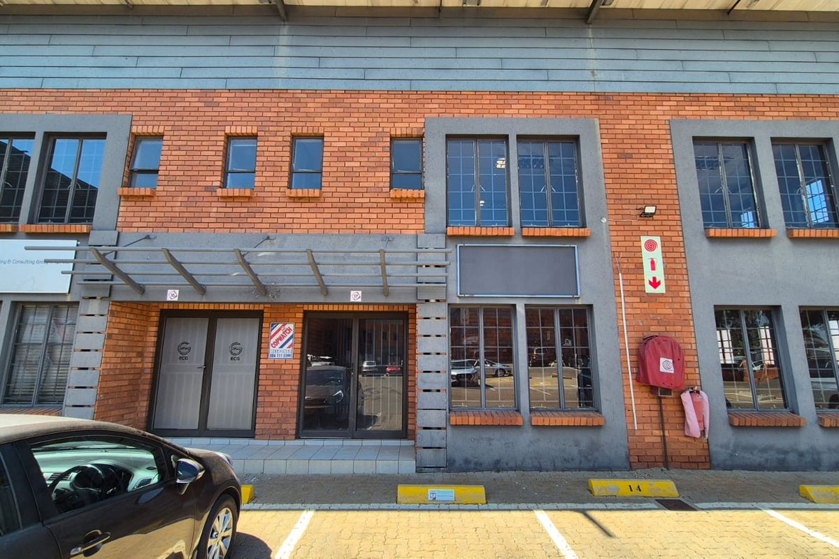 Front elevation of an industrial unit featuring a brick facade, metal-framed windows, glass entrance doors, and dedicated parking bays.