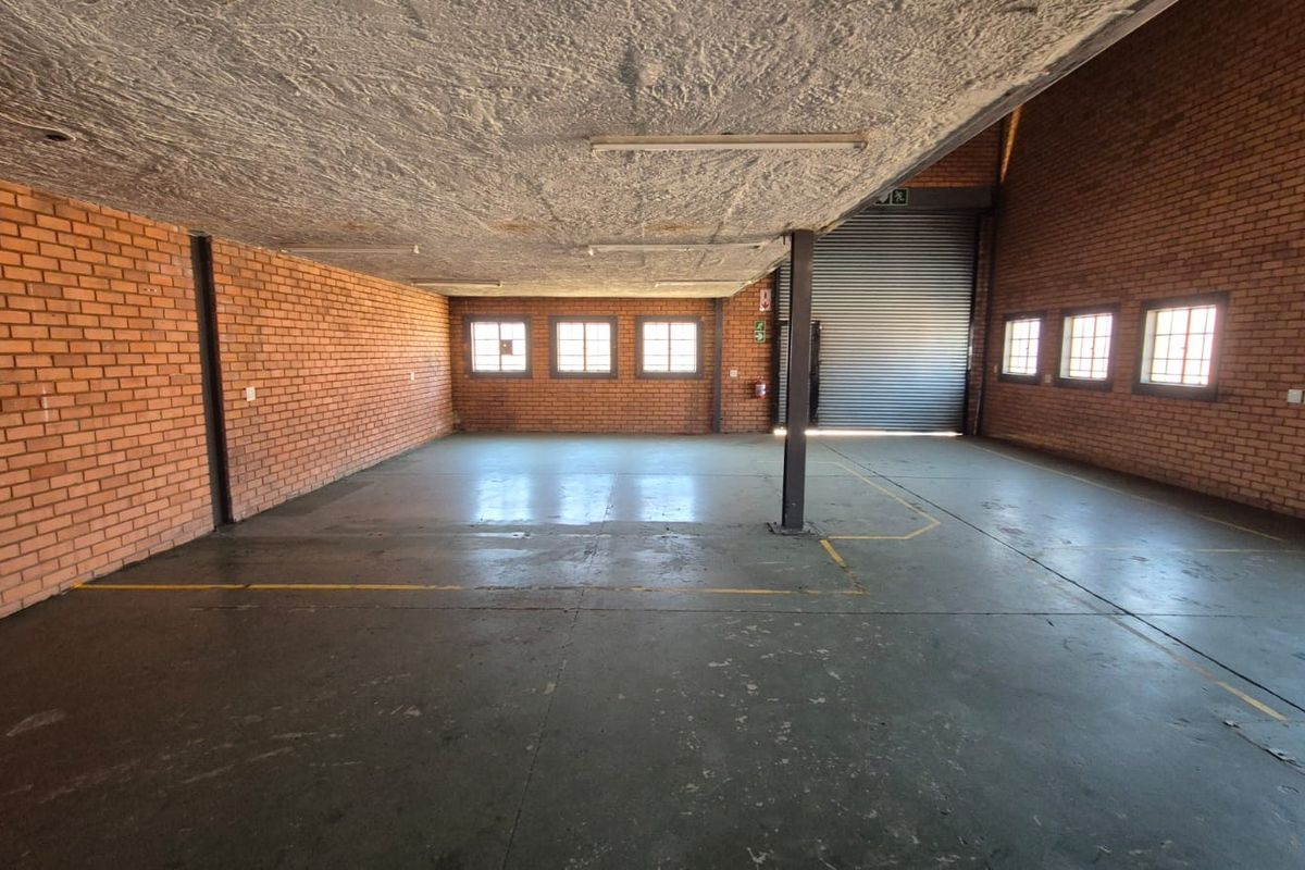 Spacious industrial utility area featuring exposed brick walls, concrete flooring, and a large roller shutter door, suitable for storage or workshop use.