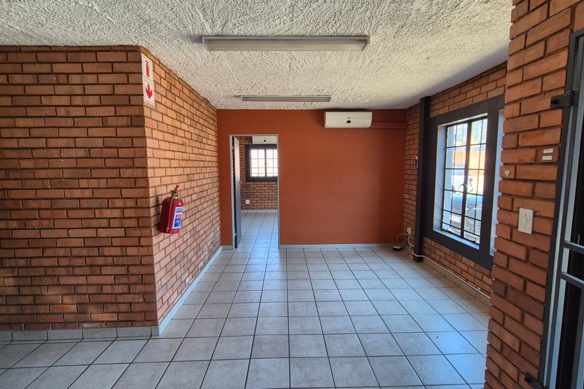 Empty office space featuring exposed brick walls, ceramic tile flooring, split-system air conditioning, and security bars on windows.
