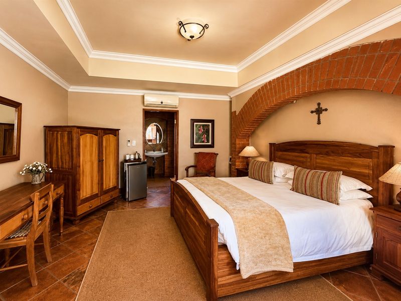 A well-maintained bedroom featuring a distinctive exposed brick archway, tray ceiling with crown molding, and terracotta floor tiles, with an adjoining en-suite bathroom.