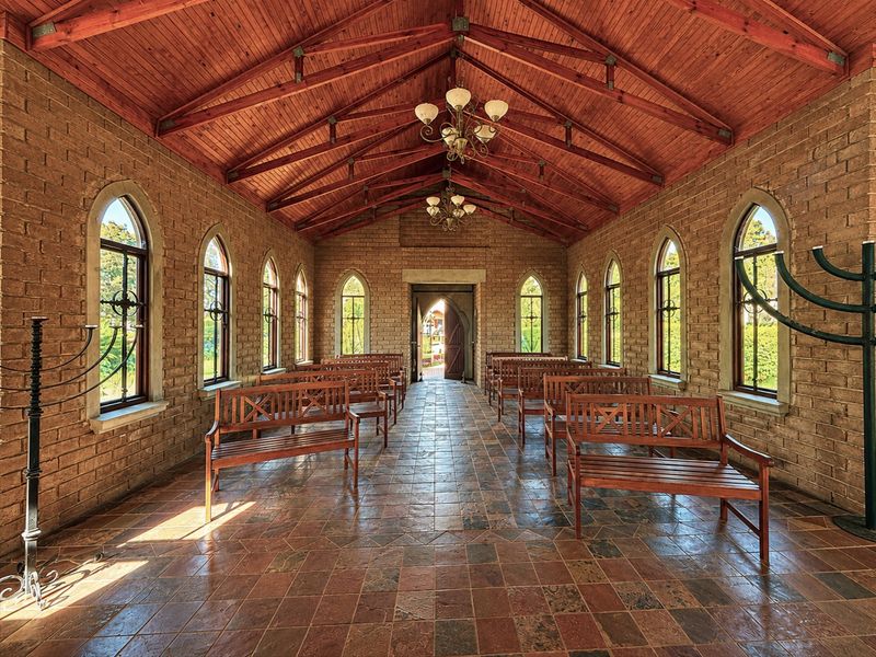 A beautifully maintained chapel or event space featuring exposed timber trusses, rustic face brick walls, arched windows, and classic tiled flooring.