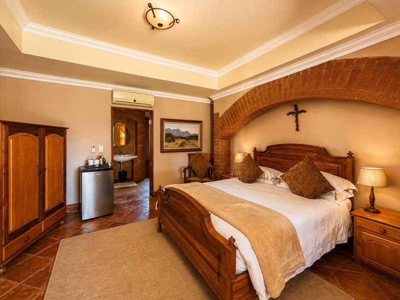 A well-maintained bedroom featuring a distinctive exposed brick archway, terracotta flooring, crown molding, and direct access to an en-suite bathroom.