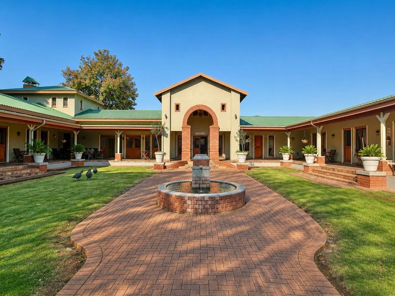 A well-maintained courtyard featuring a central brick fountain, surrounded by a covered veranda and a U-shaped building structure with green metal roofing.