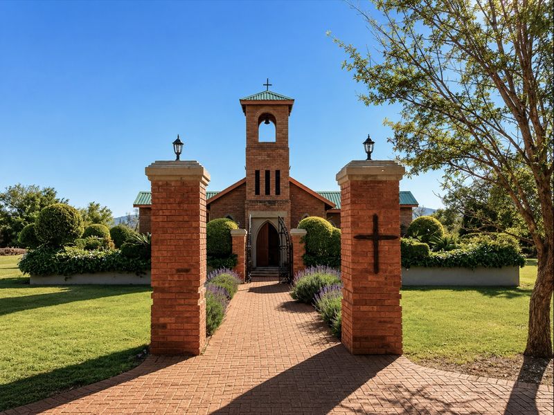 A well-maintained brick entrance pathway leading to a charming chapel building with a bell tower, surrounded by manicured gardens.