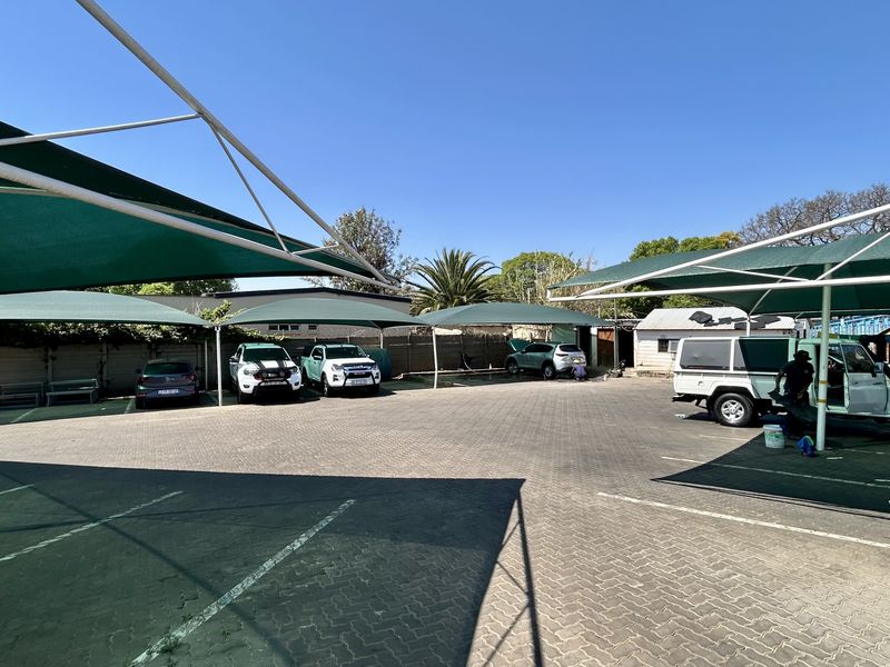 A commercial paved parking lot featuring multiple shade cloth carports and perimeter walling, providing functional outdoor vehicle storage space.