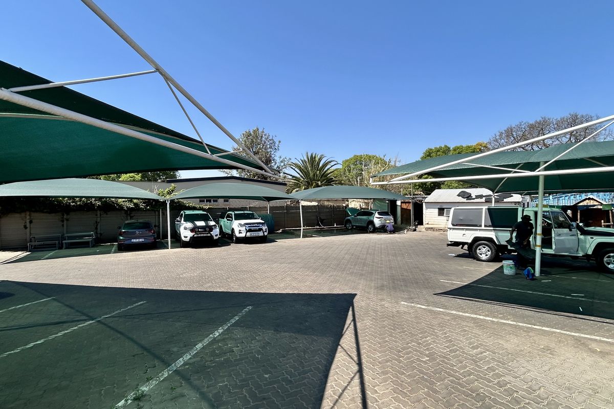 A commercial paved parking lot featuring multiple shade cloth carports and perimeter walling, providing functional outdoor vehicle storage space.