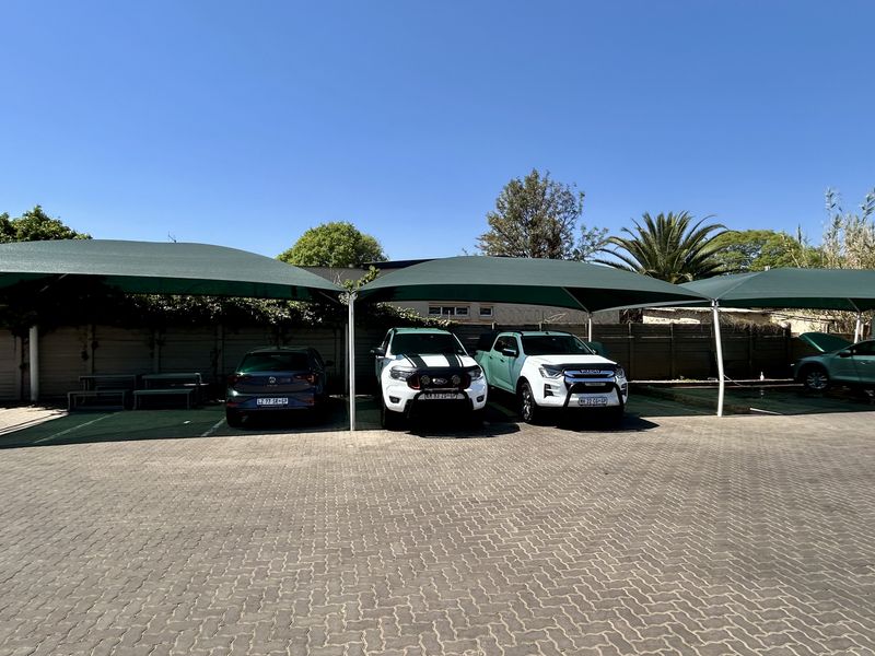 A paved commercial parking area featuring multiple shade cloth carports and a secure perimeter wall.